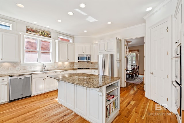 kitchen featuring white cabinets, appliances with stainless steel finishes, a center island, crown molding, and a sink