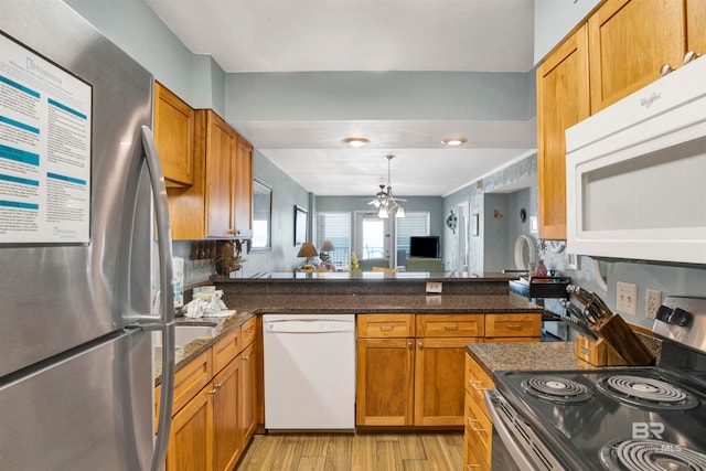 kitchen with appliances with stainless steel finishes, kitchen peninsula, light hardwood / wood-style floors, and dark stone countertops