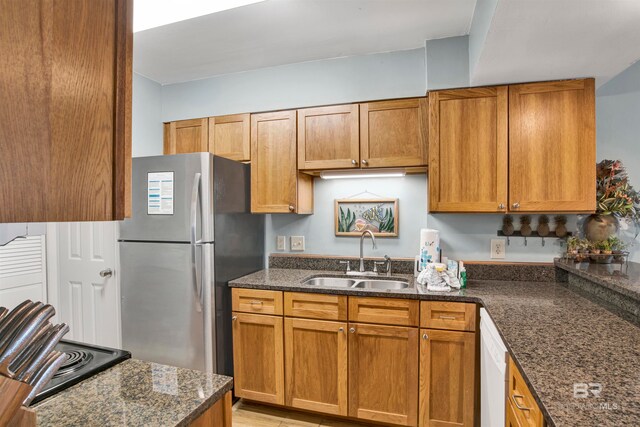 kitchen featuring dark stone counters, white dishwasher, sink, light hardwood / wood-style floors, and stainless steel refrigerator