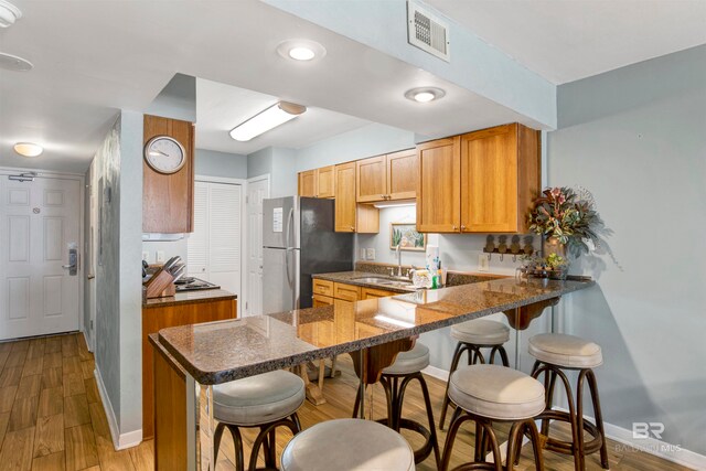 kitchen with light wood-type flooring, a kitchen bar, sink, and kitchen peninsula