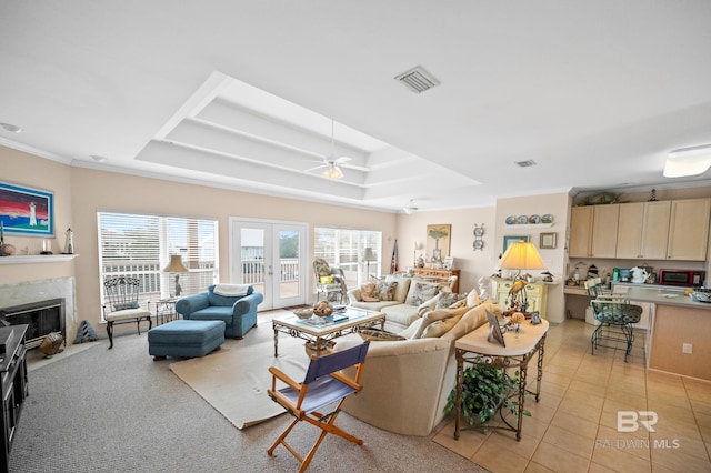 tiled living room featuring a premium fireplace, ceiling fan, a raised ceiling, and french doors