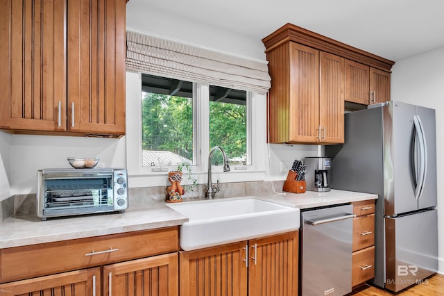 kitchen featuring a sink, appliances with stainless steel finishes, light countertops, and brown cabinetry