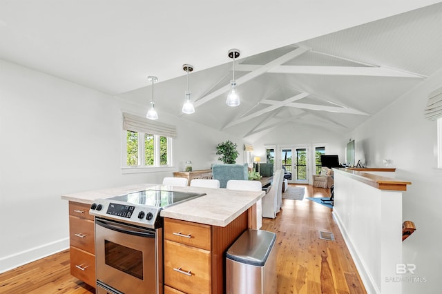 kitchen featuring stainless steel electric range oven, brown cabinetry, healthy amount of natural light, beamed ceiling, and light wood finished floors