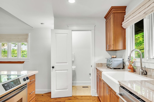 kitchen with stainless steel appliances, brown cabinets, a sink, baseboards, and light stone counters