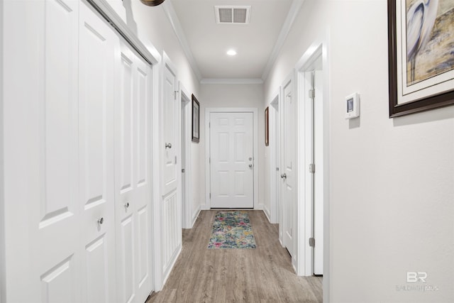 corridor with baseboards, crown molding, light wood-style flooring, and visible vents