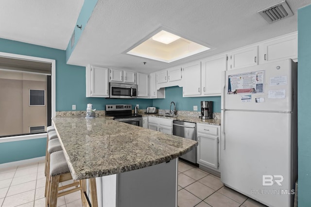 24132 Perdido Beach Blvd Unit 1081, Orange Beach, AL 36561 - kitchen with stainless steel appliances, a peninsula, a breakfast bar, light tile patterned flooring, and white cabinetry