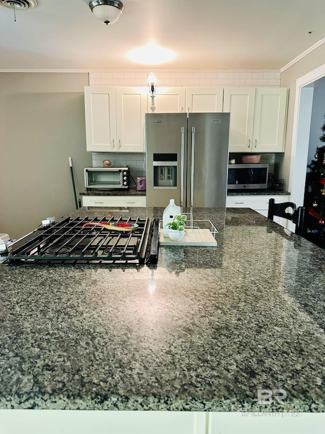 kitchen with crown molding, white cabinets, stainless steel appliances, and dark stone countertops