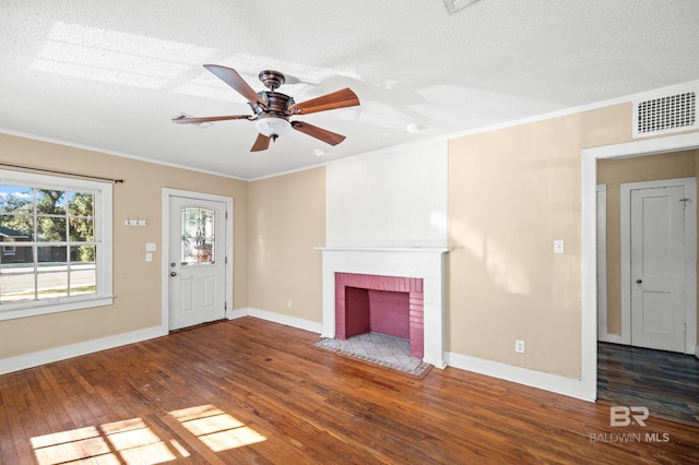 unfurnished living room featuring dark wood-type flooring, a brick fireplace, ceiling fan, ornamental molding, and a textured ceiling