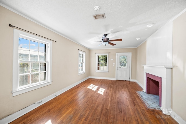 unfurnished living room featuring ceiling fan, a brick fireplace, crown molding, wood-type flooring, and a textured ceiling