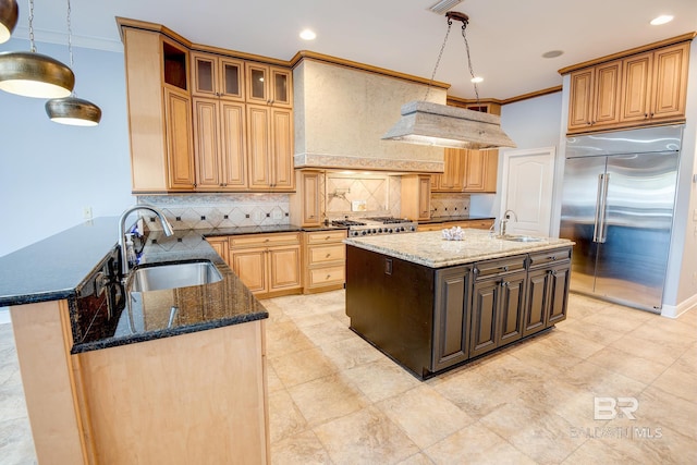 kitchen featuring dark stone countertops, a kitchen island with sink, sink, and stainless steel built in refrigerator