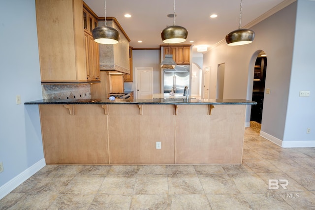 kitchen featuring hanging light fixtures, built in fridge, kitchen peninsula, dark stone countertops, and decorative backsplash