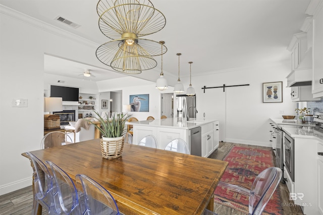 2764 W Beach Blvd, Gulf Shores, AL 36542 - dining area featuring a barn door, a glass covered fireplace, dark wood finished floors, a ceiling fan, and ornamental molding