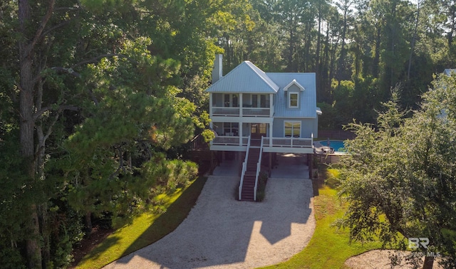 view of front facade with gravel driveway, a porch, metal roof, a view of trees, and stairs