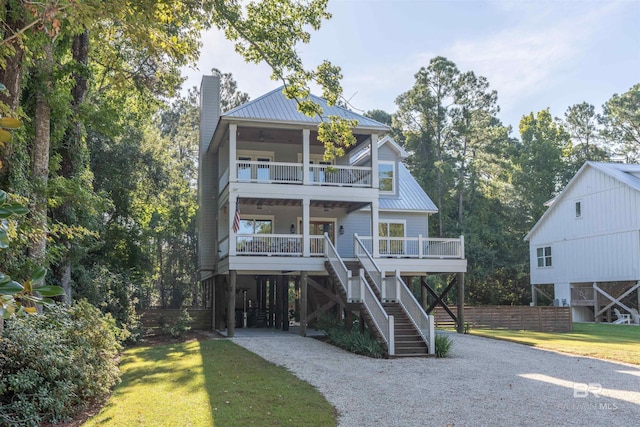 coastal home featuring metal roof, a balcony, covered porch, stairs, and gravel driveway