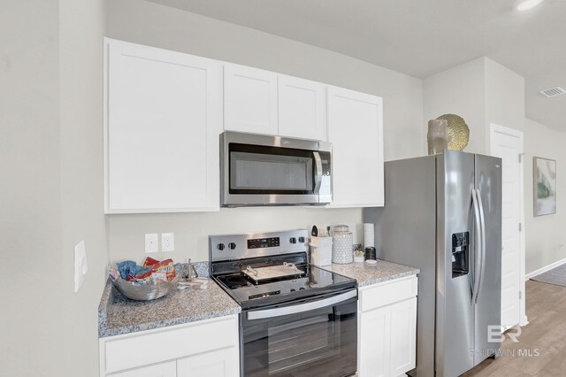 kitchen featuring white cabinets, light wood-type flooring, stainless steel appliances, and light stone counters