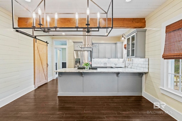 kitchen featuring pendant lighting, a barn door, wood walls, and stainless steel refrigerator with ice dispenser