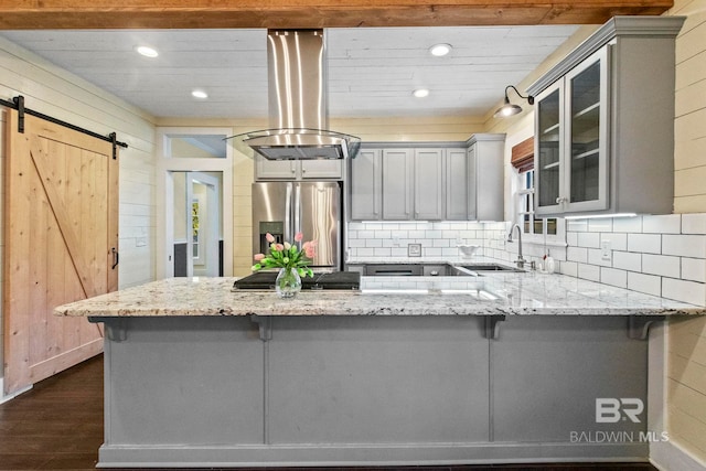 kitchen with wood walls, a barn door, light stone counters, kitchen peninsula, and stainless steel appliances