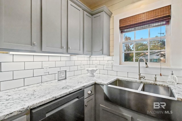 kitchen featuring backsplash, sink, stainless steel dishwasher, gray cabinets, and light stone countertops