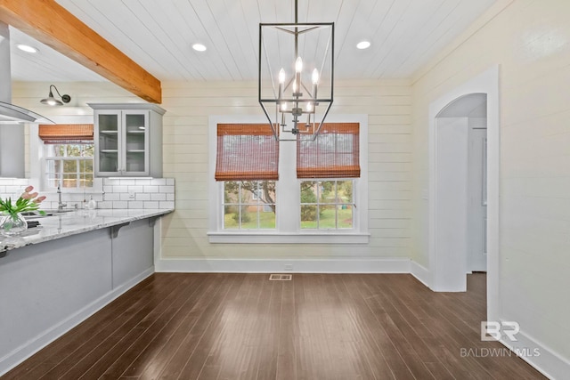 unfurnished dining area with a notable chandelier, dark hardwood / wood-style floors, beam ceiling, and wood walls