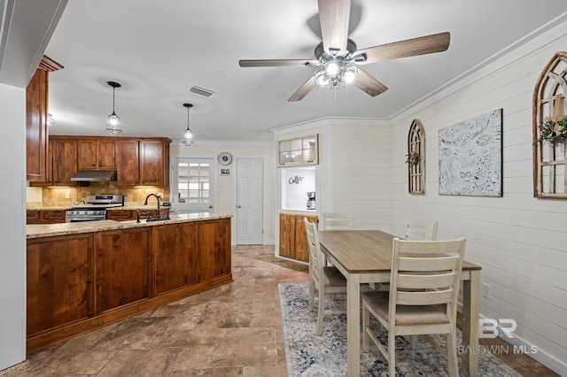 kitchen with light stone countertops, kitchen peninsula, stainless steel gas range oven, ornamental molding, and pendant lighting