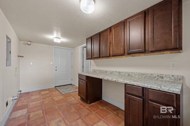 kitchen featuring dark brown cabinets, light stone counters, built in desk, and electric panel