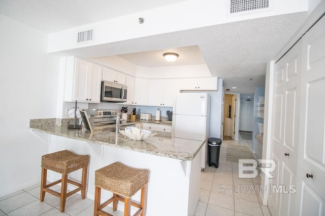 kitchen featuring a textured ceiling, a breakfast bar area, stainless steel appliances, and light stone counters