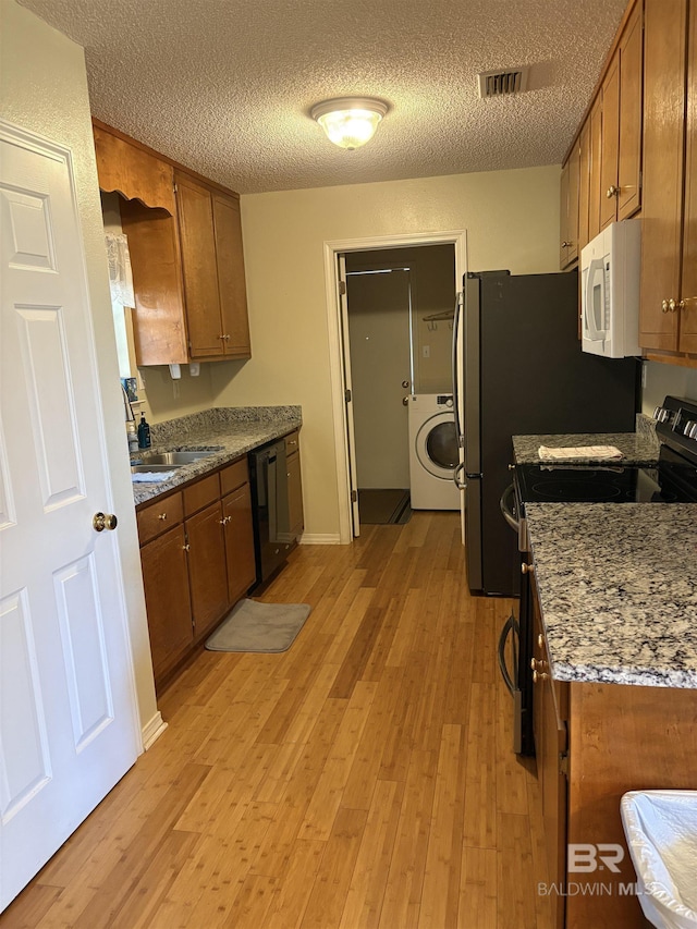 kitchen featuring visible vents, light wood-style flooring, washer / clothes dryer, brown cabinets, and stainless steel appliances