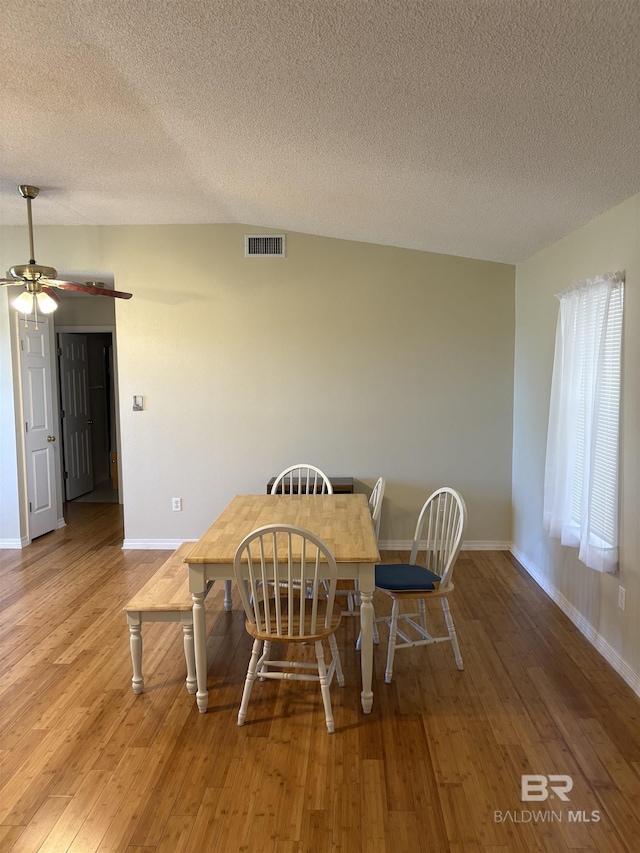 dining room featuring light wood-style flooring, a textured ceiling, visible vents, and baseboards