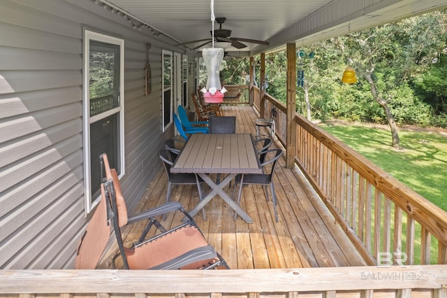 deck featuring ceiling fan, outdoor dining area, and a lawn
