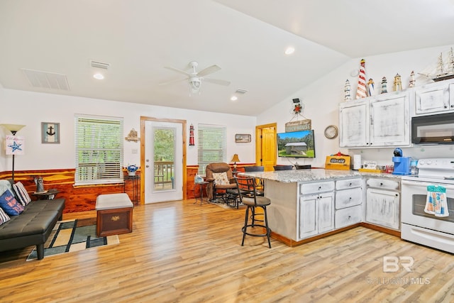 kitchen featuring a breakfast bar area, white range with electric stovetop, ceiling fan, light hardwood / wood-style flooring, and vaulted ceiling