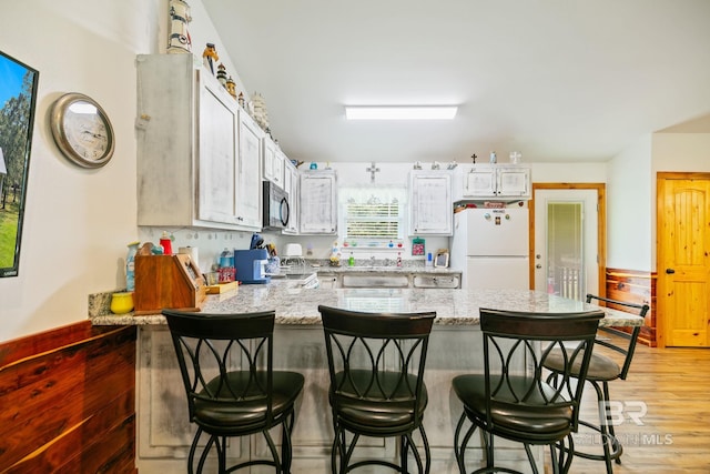 kitchen featuring freestanding refrigerator, a peninsula, light wood-type flooring, and a breakfast bar