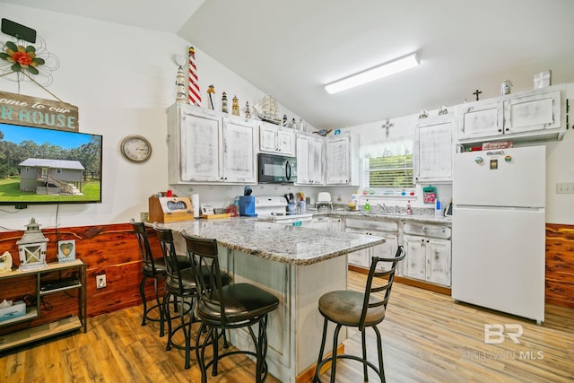 kitchen with white appliances, lofted ceiling, a peninsula, light wood finished floors, and a breakfast bar area