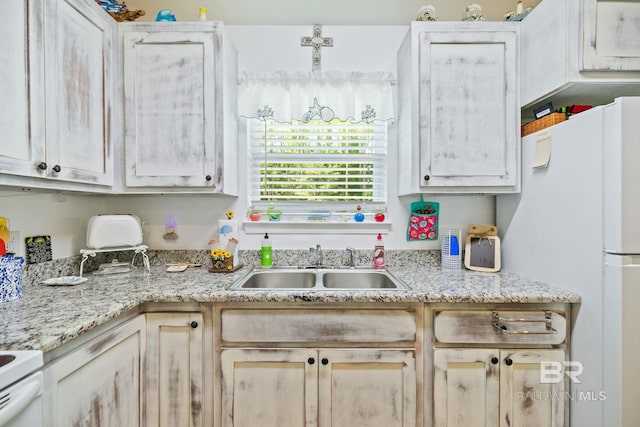 kitchen featuring light stone countertops, white refrigerator, and sink