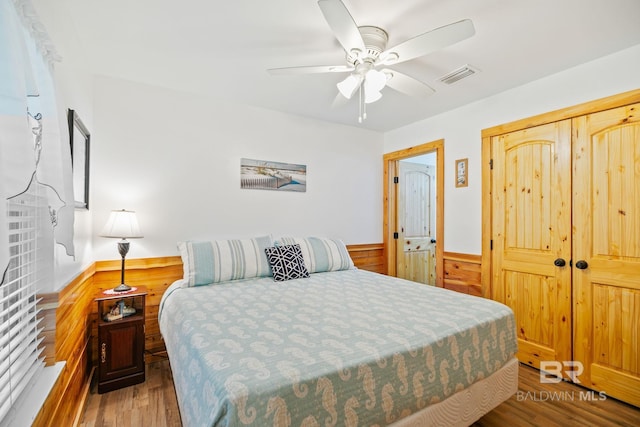 bedroom featuring wood finished floors, a wainscoted wall, a closet, wooden walls, and a ceiling fan