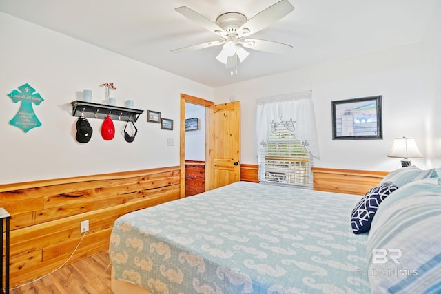 bedroom featuring wood finished floors, a wainscoted wall, wood walls, and ceiling fan