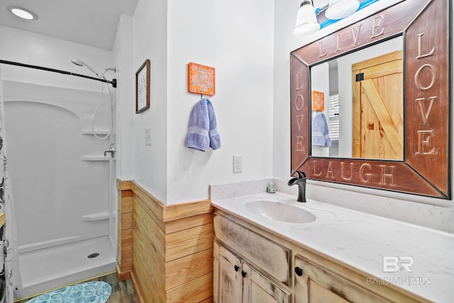 bathroom featuring vanity, a shower stall, and a wainscoted wall
