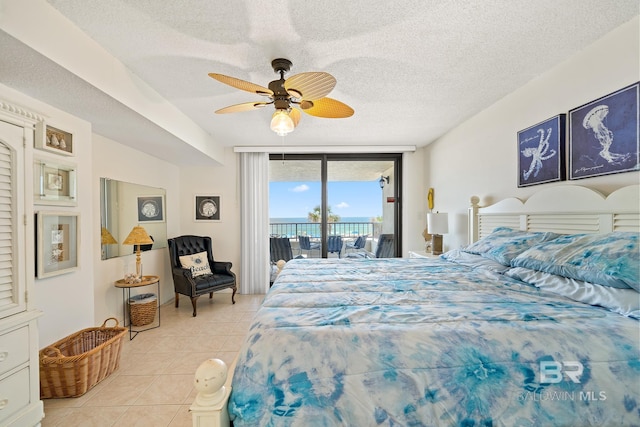 bedroom with ceiling fan, a wall of windows, a textured ceiling, access to outside, and light tile patterned floors