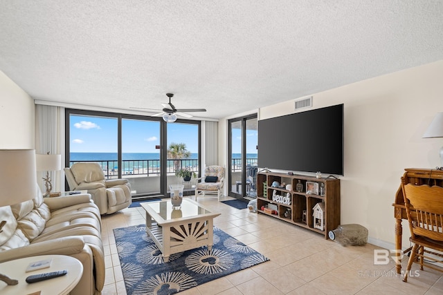 tiled living room with ceiling fan, a textured ceiling, and a wall of windows