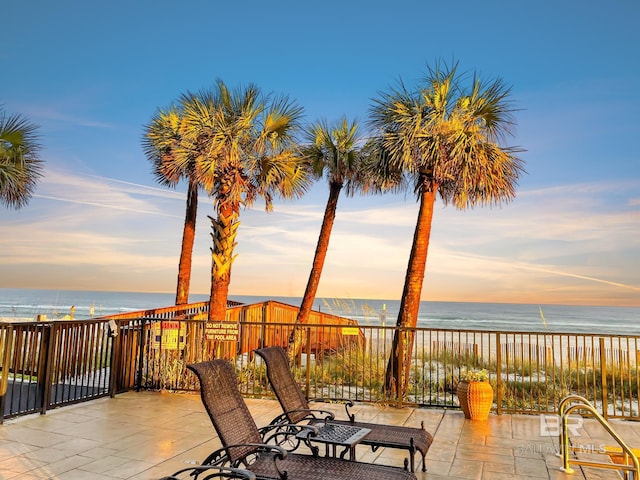 patio terrace at dusk featuring a water view and a view of the beach