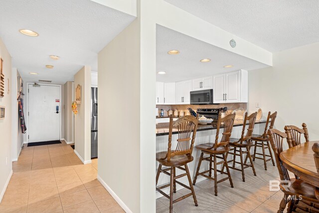 kitchen with a kitchen bar, appliances with stainless steel finishes, backsplash, light tile patterned floors, and white cabinetry