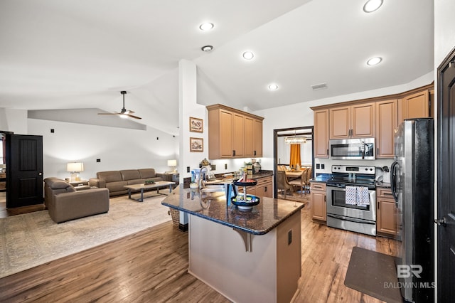 kitchen with appliances with stainless steel finishes, light hardwood / wood-style flooring, vaulted ceiling, and a breakfast bar area