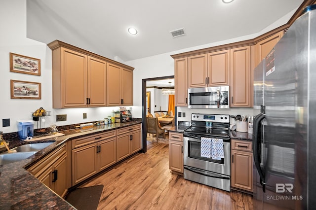 kitchen featuring lofted ceiling, dark stone counters, sink, appliances with stainless steel finishes, and light hardwood / wood-style floors