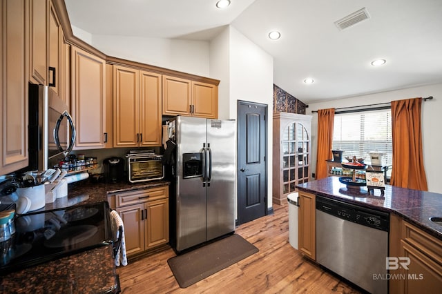 kitchen with dark stone countertops, light hardwood / wood-style flooring, stainless steel appliances, and lofted ceiling