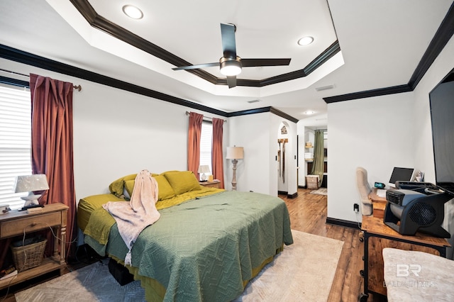 bedroom with light wood-type flooring, a raised ceiling, ceiling fan, and crown molding