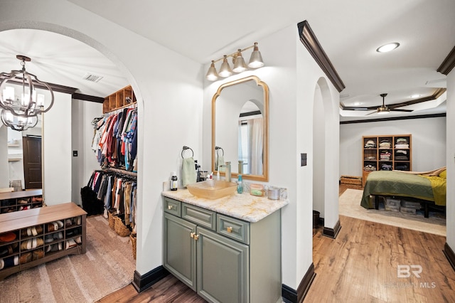 bathroom with hardwood / wood-style floors, a tray ceiling, vanity, ceiling fan with notable chandelier, and ornamental molding