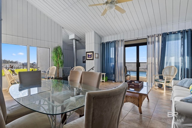 tiled dining space featuring ceiling fan, wooden walls, and a water view