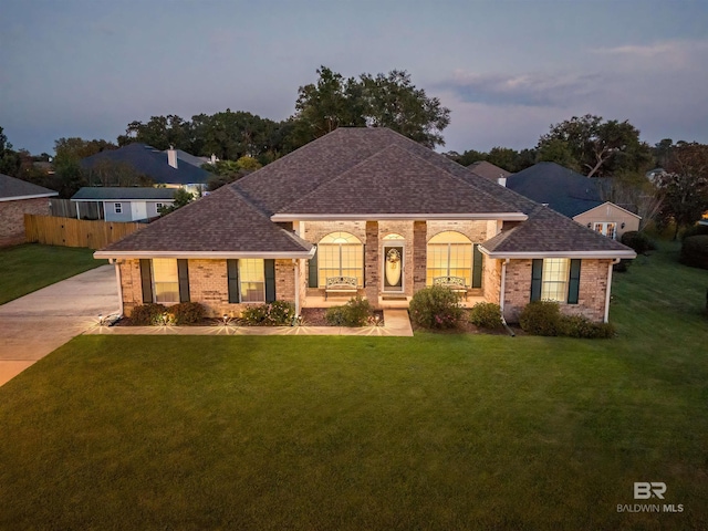 single story home featuring a front lawn, fence, brick siding, and roof with shingles