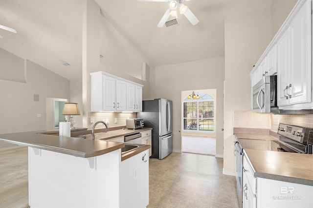 kitchen with a ceiling fan, appliances with stainless steel finishes, a peninsula, white cabinets, and decorative backsplash