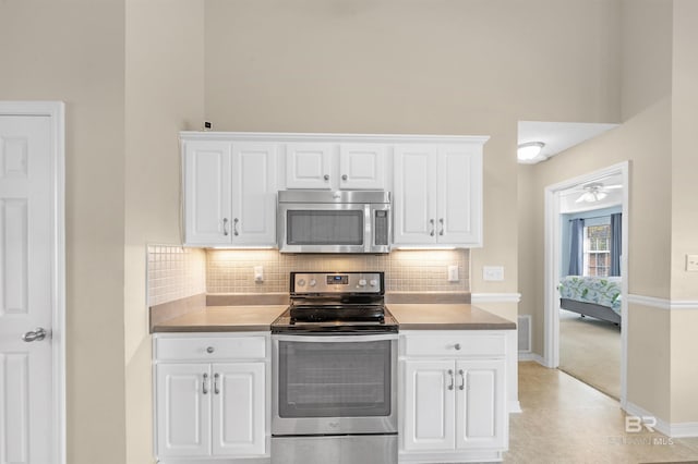 kitchen featuring visible vents, decorative backsplash, appliances with stainless steel finishes, a towering ceiling, and white cabinets