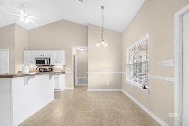 kitchen with visible vents, a breakfast bar, pendant lighting, stainless steel microwave, and ceiling fan with notable chandelier